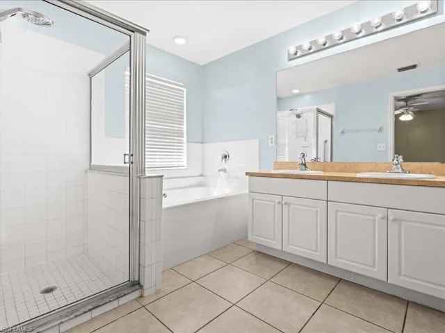 Master Full bath with double vanity, light tile patterned floors, a bath, a stall shower, and a ceiling fan