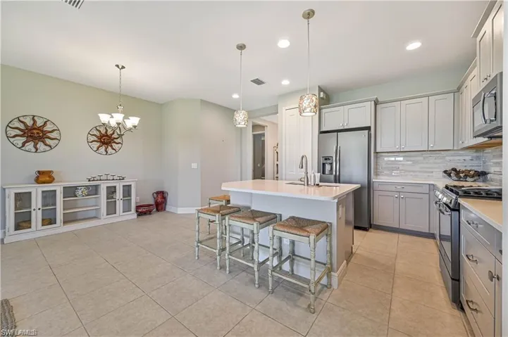 Kitchen featuring a kitchen island with sink, pendant lighting, a kitchen breakfast bar, backsplash, and appliances with stainless steel finishes