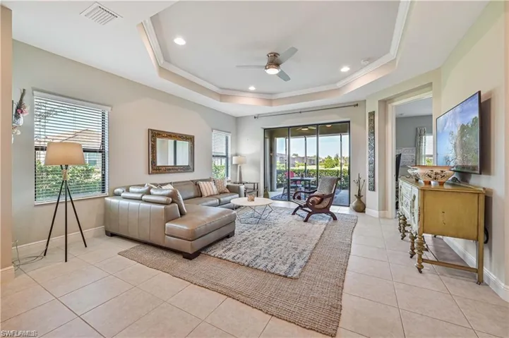 Tiled living room with ceiling fan, a tray ceiling, and crown molding