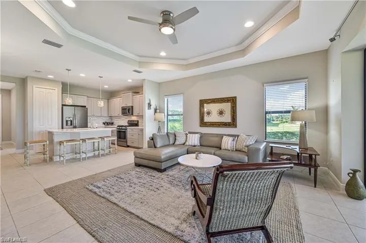 Living room featuring crown molding, a tray ceiling, light tile patterned floors, and ceiling fan