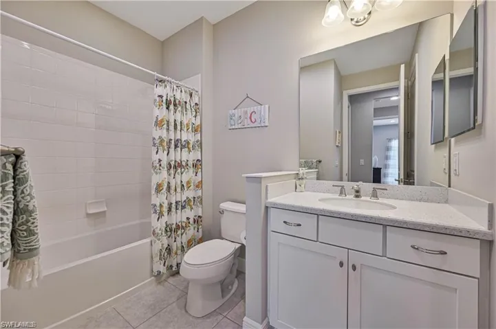 Full bathroom featuring shower / tub combo with curtain, tile patterned floors, vanity, and toilet