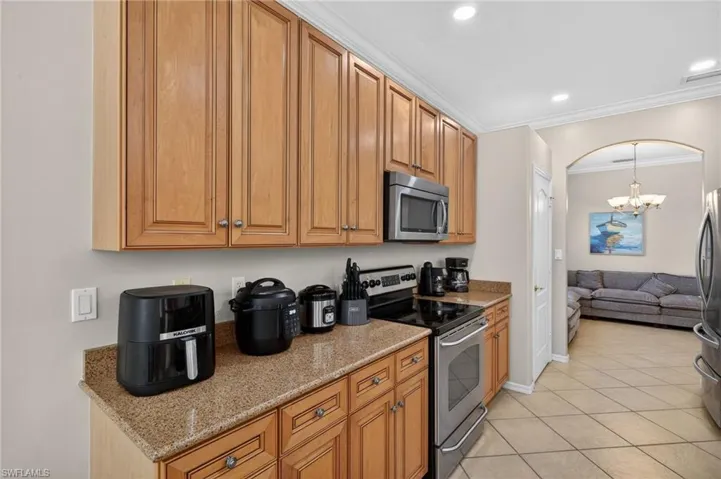 Kitchen with stainless steel appliances, light stone counters, crown molding, wood finish cabinetry, and suspended lighting