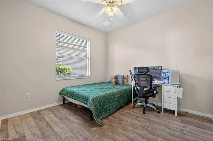 Bedroom with wood finished floors, a ceiling fan, and an office area