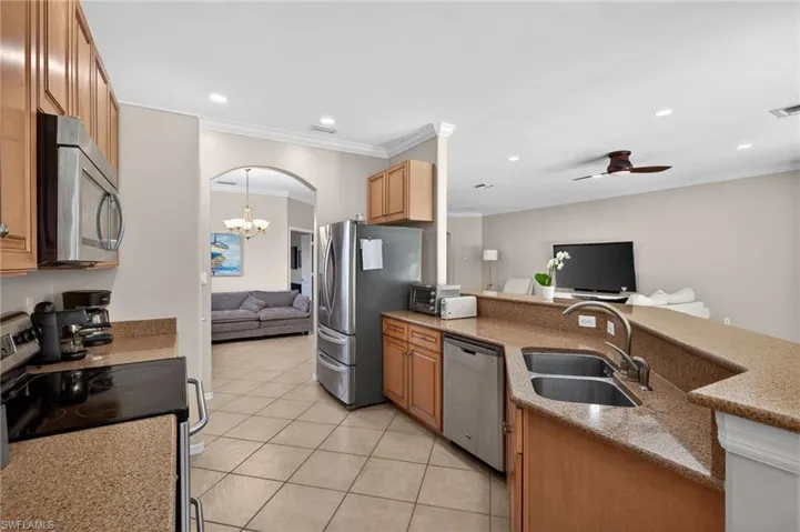 Kitchen featuring arched walkways, stainless steel appliances, open floor plan, ornamental molding, and a peninsula