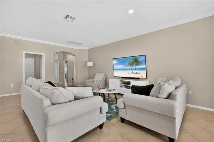 Living room featuring arched walkways, light tile patterned floors, ornamental molding, and recessed lighting