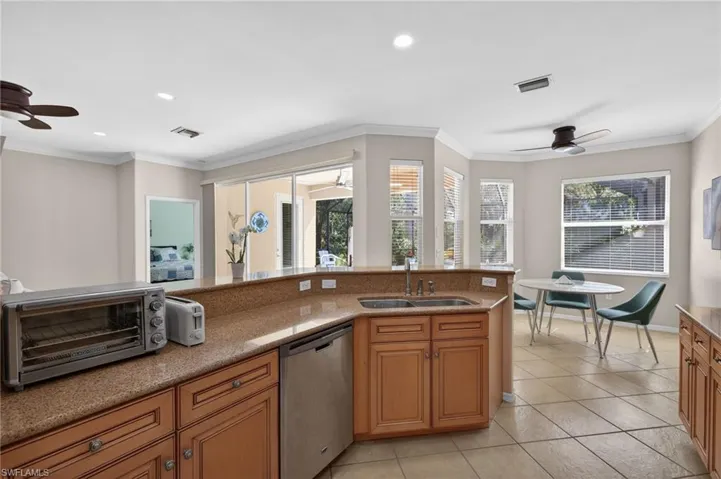 Kitchen featuring ceiling fan, wood finish cabinets, dishwasher, crown molding, and light stone counters