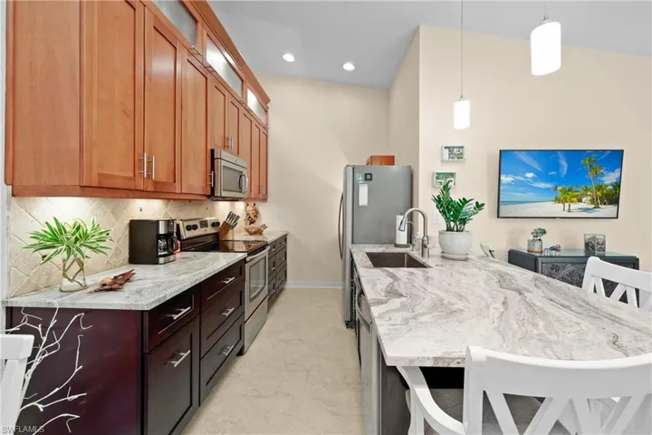 Kitchen featuring a kitchen breakfast bar, light stone countertops, hanging light fixtures, and appliances with stainless steel finishes