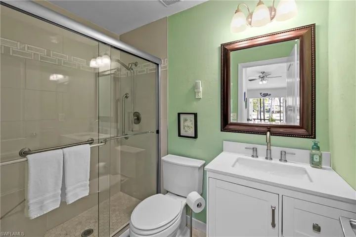 Bathroom with vanity, ceiling fan with notable chandelier, toilet, and a shower with door