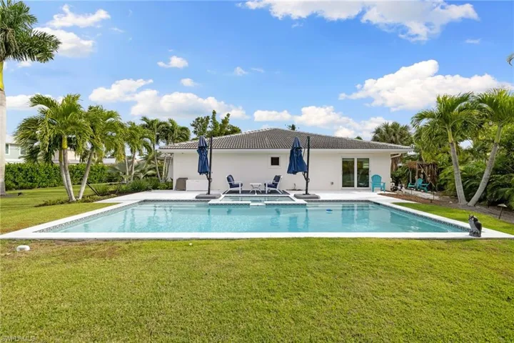 Rear view of property with a yard, a patio area, a pool with connected hot tub, stucco siding, and a tiled roof