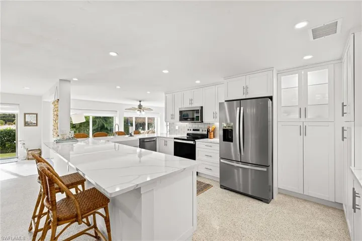 Kitchen with stainless steel appliances, a breakfast bar, a peninsula, white cabinetry, and light stone countertops