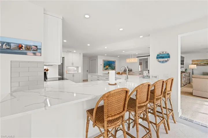Kitchen with white cabinetry, light stone countertops, a peninsula, a kitchen breakfast bar, and recessed lighting