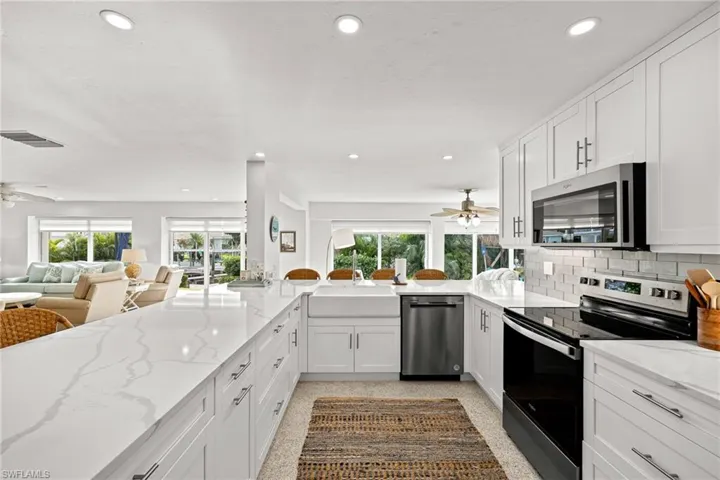 Kitchen featuring a ceiling fan, stainless steel appliances, light stone countertops, white cabinets, and recessed lighting