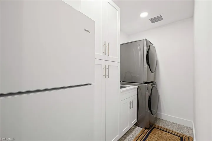 Washroom with stacked washer and clothes dryer, cabinet space, dark aggregate flooring, and recessed lighting