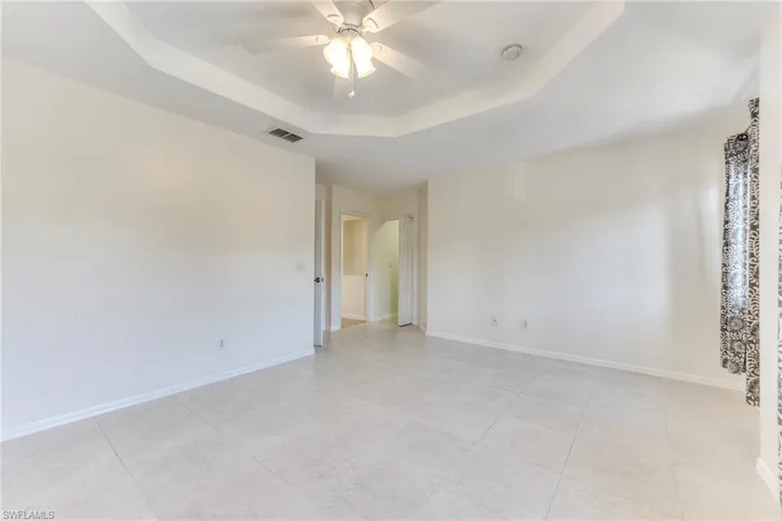 Master bedroom with a tray ceiling, a ceiling fan, light tile patterned floors, and a smoke detector