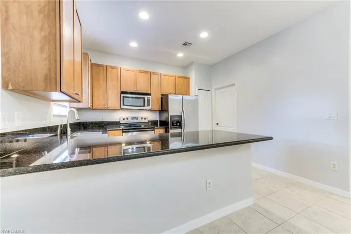 Kitchen featuring appliances with stainless steel finishes, a peninsula, dark stone countertops, recessed lighting, and light tile patterned floors