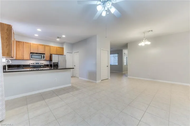 Kitchen featuring stainless steel appliances, dark countertops, a peninsula, ceiling fan, and brown cabinetry
