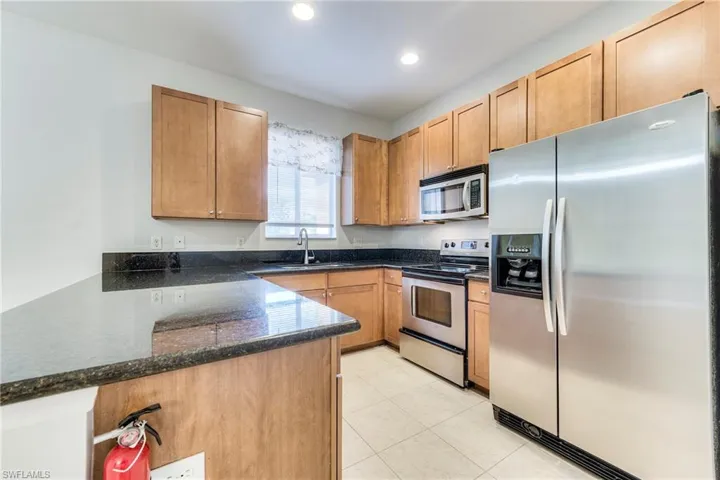 Kitchen with appliances with stainless steel finishes, a peninsula, dark stone countertops, light tile patterned flooring, and recessed lighting