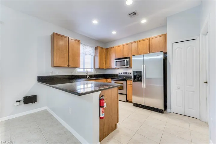 Kitchen with appliances with stainless steel finishes, a peninsula, light tile patterned floors, recessed lighting, and brown cabinets
