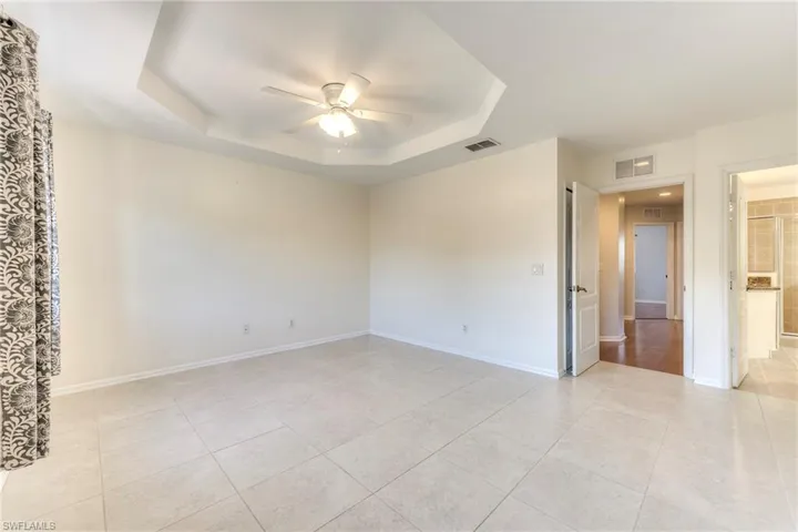 Master bedroom with ceiling fan, a tray ceiling, and light tile patterned floors