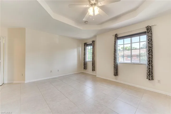 Master bedroom featuring a raised ceiling, light tile patterned floors, and ceiling fan