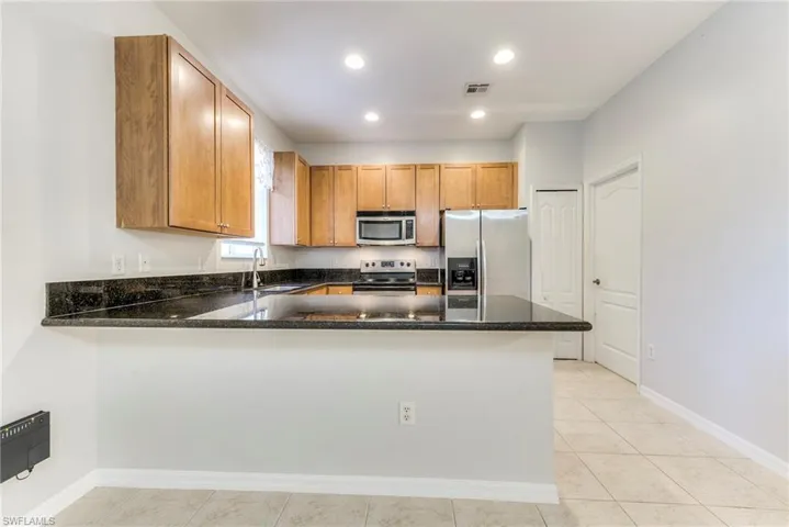 Kitchen with stainless steel appliances, a peninsula, dark stone counters, recessed lighting, and brown cabinetry