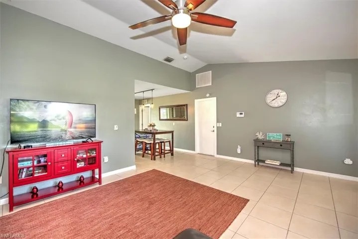 Living room with lofted ceiling, ceiling fan, and light tile floors