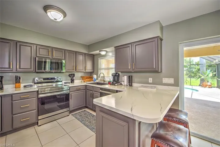 Kitchen with kitchen peninsula, light stone counters, sink, a breakfast bar, and appliances with stainless steel finishes