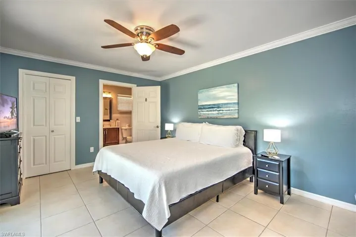 Bedroom featuring crown molding, ceiling fan, light tile floors, and ensuite bath
