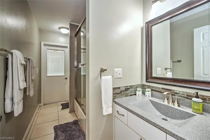 Bathroom featuring enclosed tub / shower combo, vanity, tasteful backsplash, and tile floors