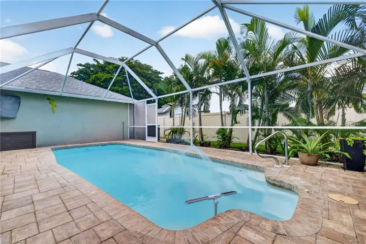 Screened pool enclosure featuring a rectangular pool, paver deck, and surrounding tropical landscaping