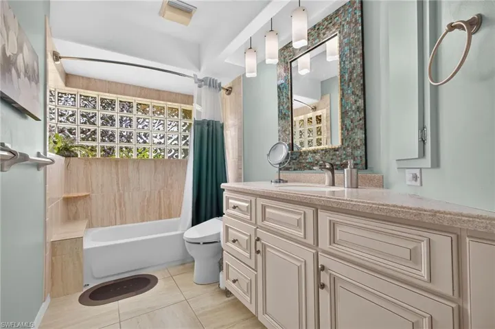 Vanity with light-toned countertop and integrated sink, pendant lighting, glass block window, and tiled shower surround with built-in bench