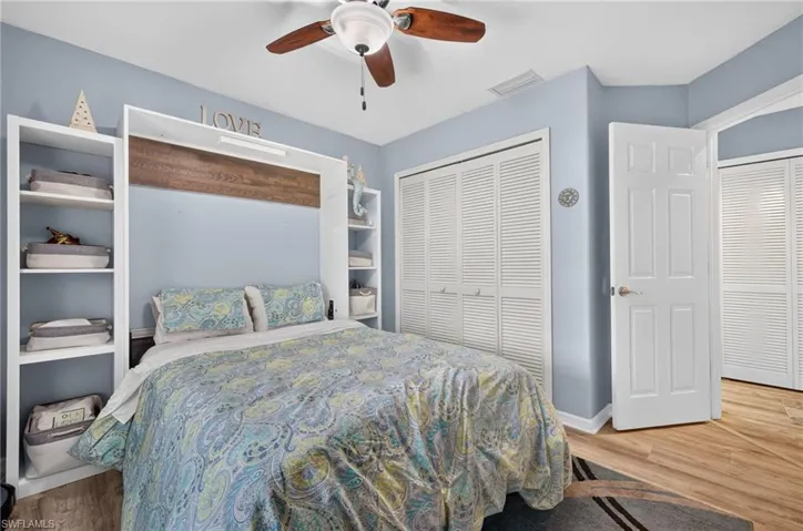 Integrated wall-mounted bed with flanking open shelving, wood-finish flooring, two sets of bi-fold louvered closet doors, and a ceiling fan with light fixture