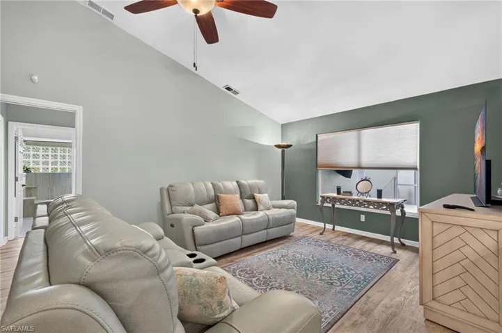 Vaulted ceiling with a ceiling fan, wood-finish flooring, and a large window with roller shades