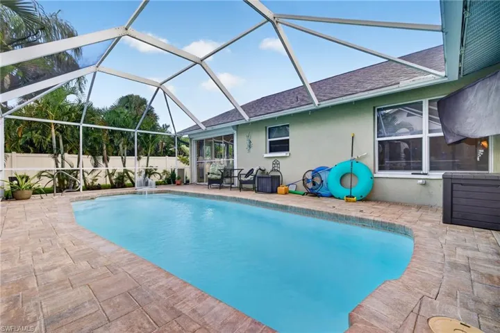 Screened-in swimming pool with a water feature, surrounded by paver decking