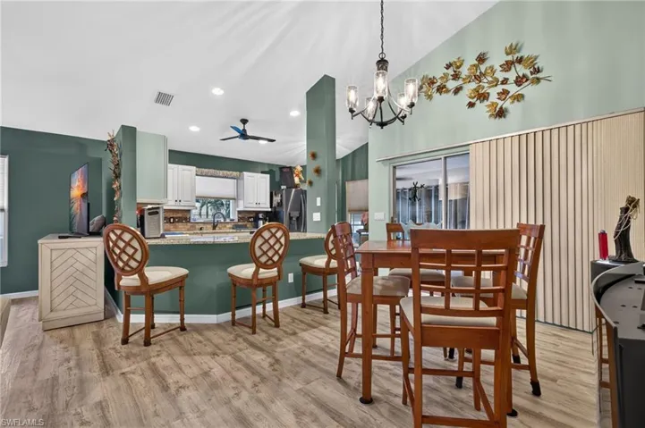 Kitchen area featuring wood-finish flooring, a kitchen island with stone countertop, white shaker cabinetry, a ceiling fan, and a chandelier