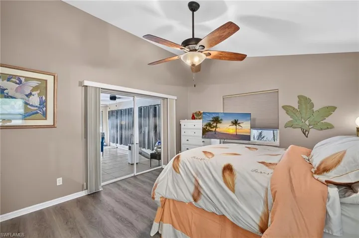 Vaulted ceiling with a ceiling fan, wood-finish flooring, sliding glass doors, and a window with a roller shade