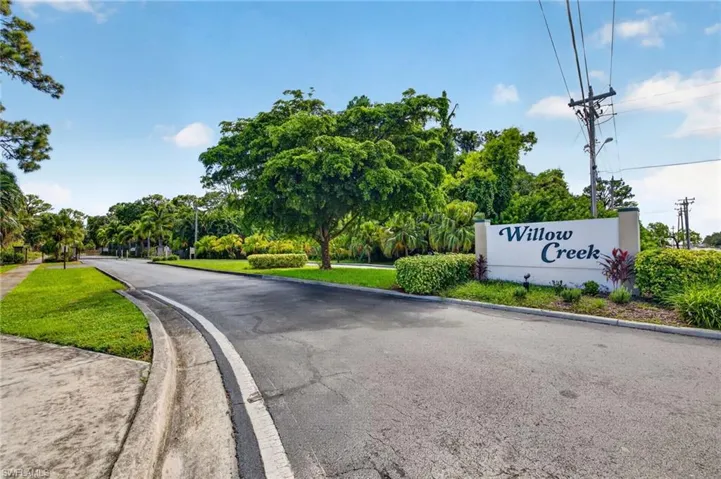 Entry monument sign with raised lettering, surrounded by mature landscaping and a well-maintained asphalt road
