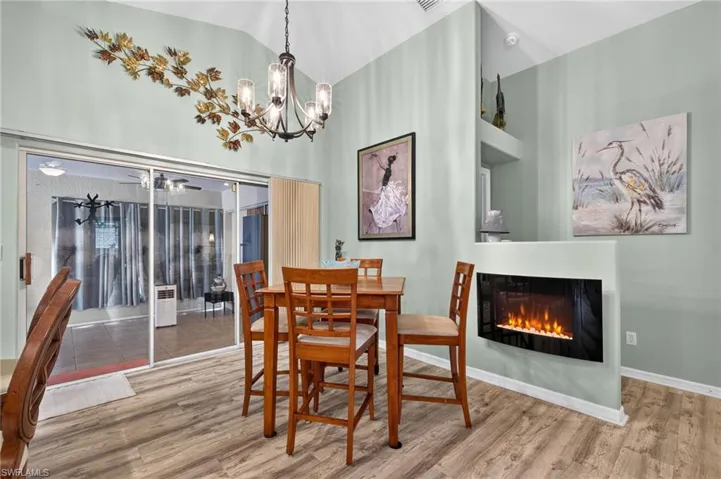 Vaulted ceiling with an installed chandelier, wood-finish flooring, built-in fireplace, and sliding glass door