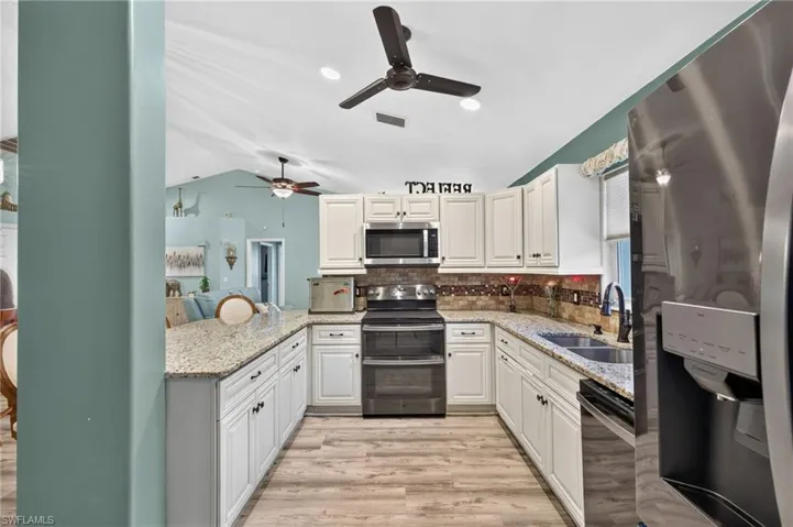 U-shaped kitchen featuring white cabinetry, light-toned countertops, stainless steel appliances, and a tile backsplash