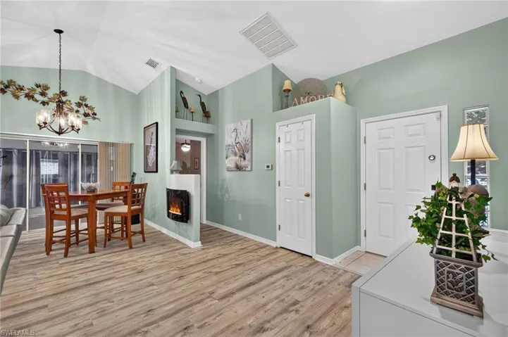 Vaulted ceiling with a decorative chandelier, wood-finish flooring, and an electric fireplace feature