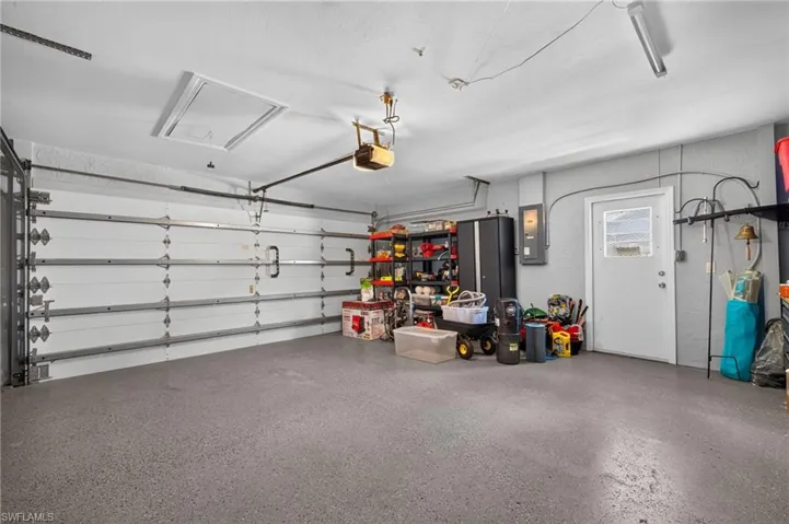 Garage with a finished concrete floor, overhead lighting, an automatic garage door opener, and a side access door