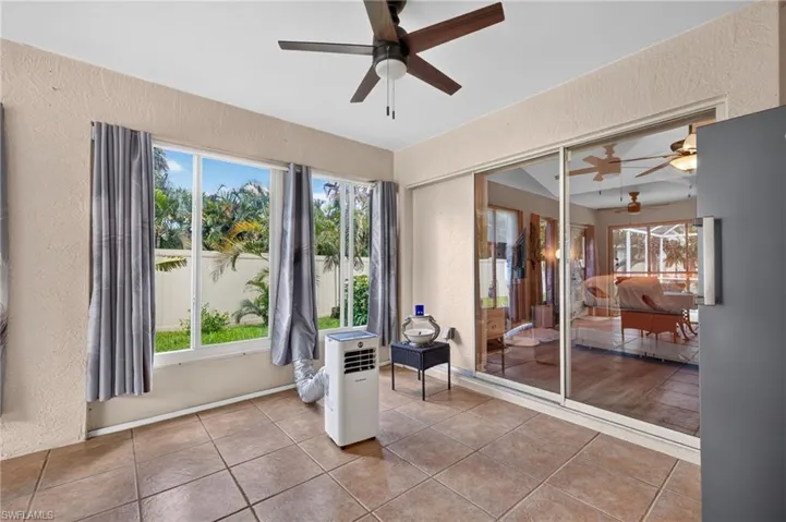 Tiled flooring, multiple windows, sliding glass doors, textured walls, and a ceiling fan