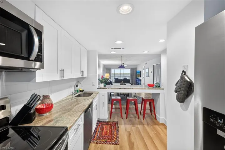 Kitchen featuring stainless steel appliances, white cabinets, light wood-style floors, decorative backsplash, and recessed lighting