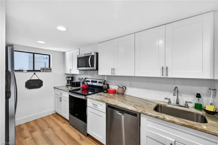 Kitchen with stainless steel appliances, white cabinets, light wood-style flooring, light stone counters, and recessed lighting