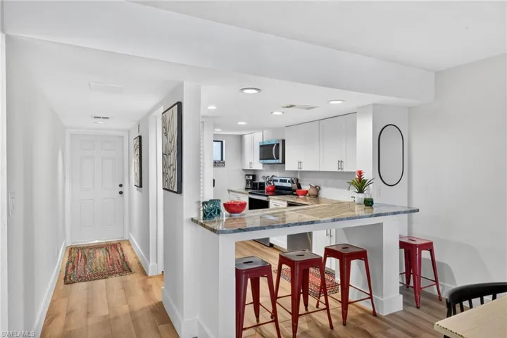 Kitchen featuring dark stone countertops, a breakfast bar, stainless steel appliances, light wood finished floors, and recessed lighting