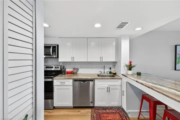 Kitchen featuring light stone counters, stainless steel appliances, white cabinetry, light wood finished floors, and recessed lighting