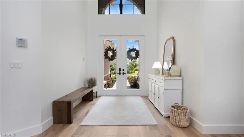 Entryway with french doors, light wood finished floors, a towering ceiling, and baseboards