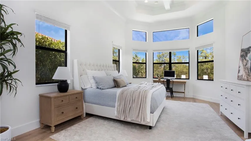 Bedroom with ornamental molding, light wood-style floors, baseboards, and a raised ceiling