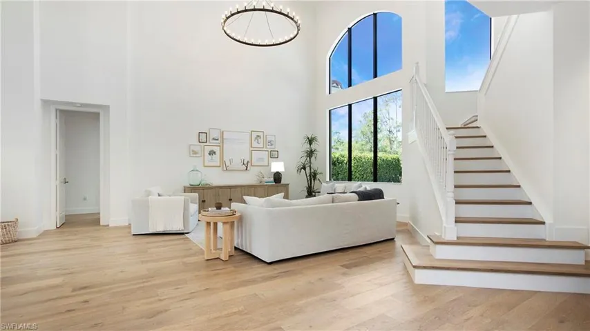Living area with a towering ceiling, stairs, light wood-type flooring, a chandelier, and baseboards