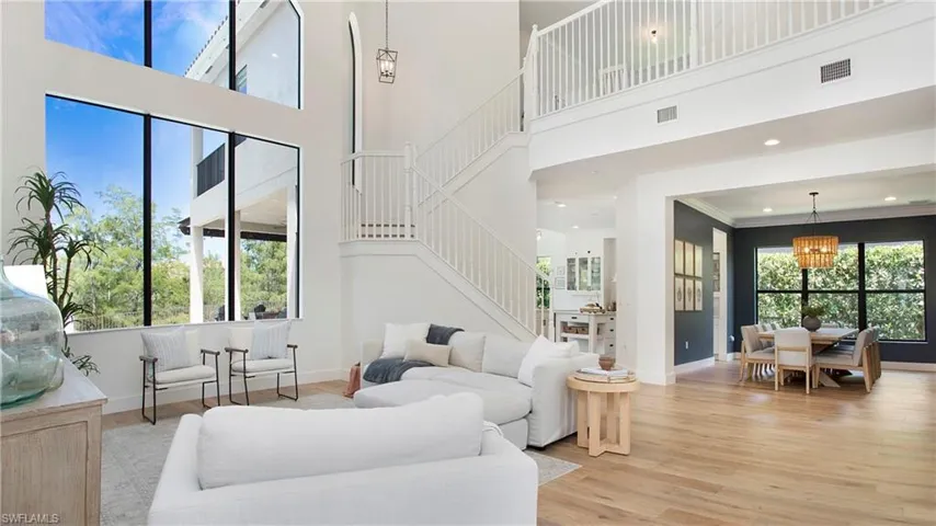 Living room featuring stairs, baseboards, light wood-style flooring, a chandelier, and a towering ceiling